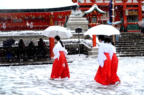 雪が積もる境内を歩く巫女さん